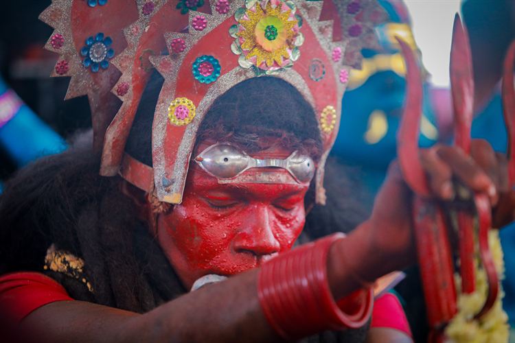 A performer in a red painted face and an ornate festival headdress
