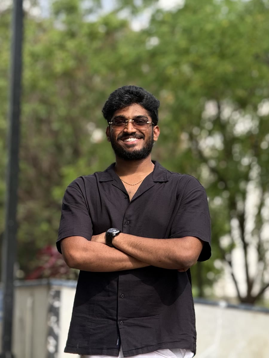 Vigneshwaran, arms crossed and smiling, standing outdoors in front of trees